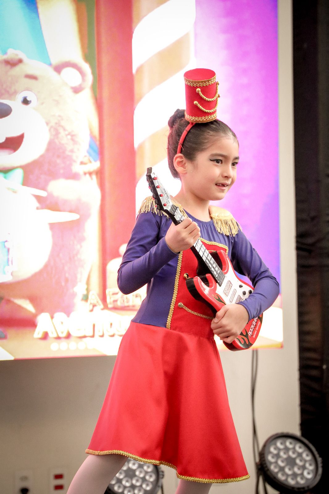 Bailarina em fantasia vermelha de soldadinho com guitarra no palco